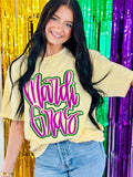 A person wearing a yellow t-shirt with neon purple and green glitter, and the text 'MARDI GRAS' in cursive script.