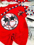 A red graphic tee with a baseball and stars design, accompanied by blue and white beaded necklaces and a black hair tie.