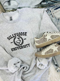 A gray embroidered sweatshirt with 'Silly Goose University' text on the front, paired with white sneakers with embellishments on the sole.