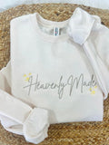 White sweatshirt with 'Heavenly Made' text on a woven surface