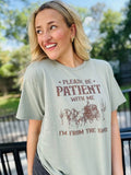 A woman wearing a green short-sleeved graphic tee with the text 'Please be patient with me I'm from the 1900's' printed on it, standing outdoors.