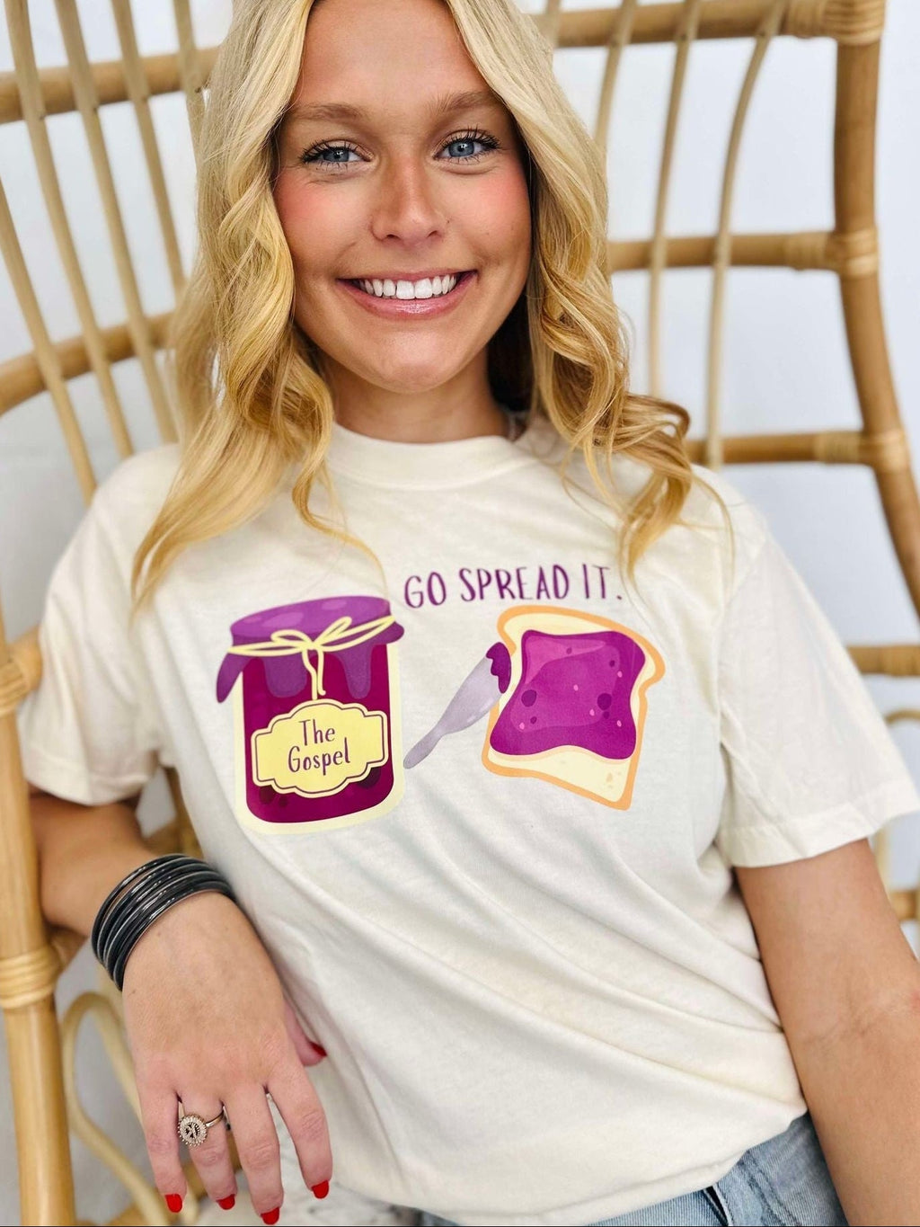 Person wearing a white t-shirt with graphics and text "Go spread it", sitting on a wicker chair.