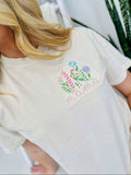 A woman wearing a white short-sleeved t-shirt with embroidered floral design and the word 'mama' on the front.