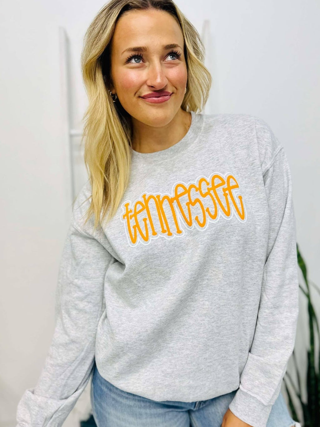 Woman wearing a gray sweatshirt with 'Tennessee' in yellow text, standing indoors.