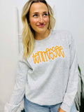 Woman wearing a gray sweatshirt with 'Tennessee' in yellow text, standing indoors.