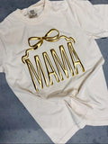 An ivory colored t-shirt with the word 'MAMA' printed in gold metallic vinyl in a bow shape.