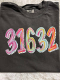 A folded black t-shirt with the zip code '31632' painted in various colors on the front.