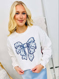 A woman wearing a white sweatshirt with a blue Chino bow graphic design on the front.