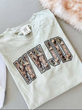 A white t-shirt with 'WWJD' camouflage pattern printed on it, displayed flat with a tag and a furry item in the background.