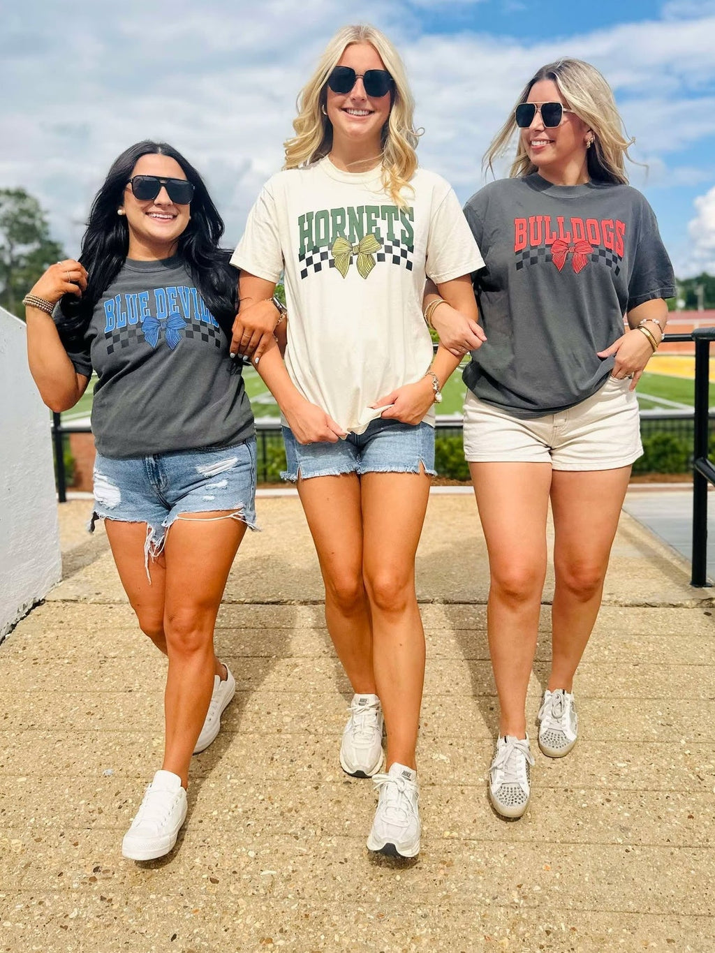 Three women wearing sports team t-shirts walking together outdoors on a sunny day.