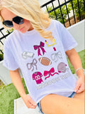 Person wearing a white t-shirt with colorful football and bow with goal graphics and text, sitting outdoors.