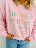 Person wearing a pink sweatshirt with colorful text design, the maker of heaven calls me HIS, standing against a plain background.