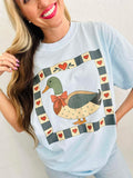 Woman wearing a light blue t-shirt with a duck mallard patchwork graphic design.