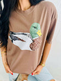 Person wearing a brown t-shirt with a viral patchwork mallard duck graphic design.