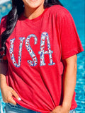 A person wearing a red t-shirt with the text 'USA' and an embroidered design resembling a flag on it, standing by a pool.