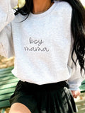 Child wearing a gray sweatshirt with 'boy mama' text, sitting on a green bench.