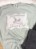 Light green t-shirt with Duck Hunting Wives Social Club graphic design on a textured surface