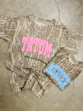 Camouflage t-shirt with pink text and blue shorts on a concrete floor