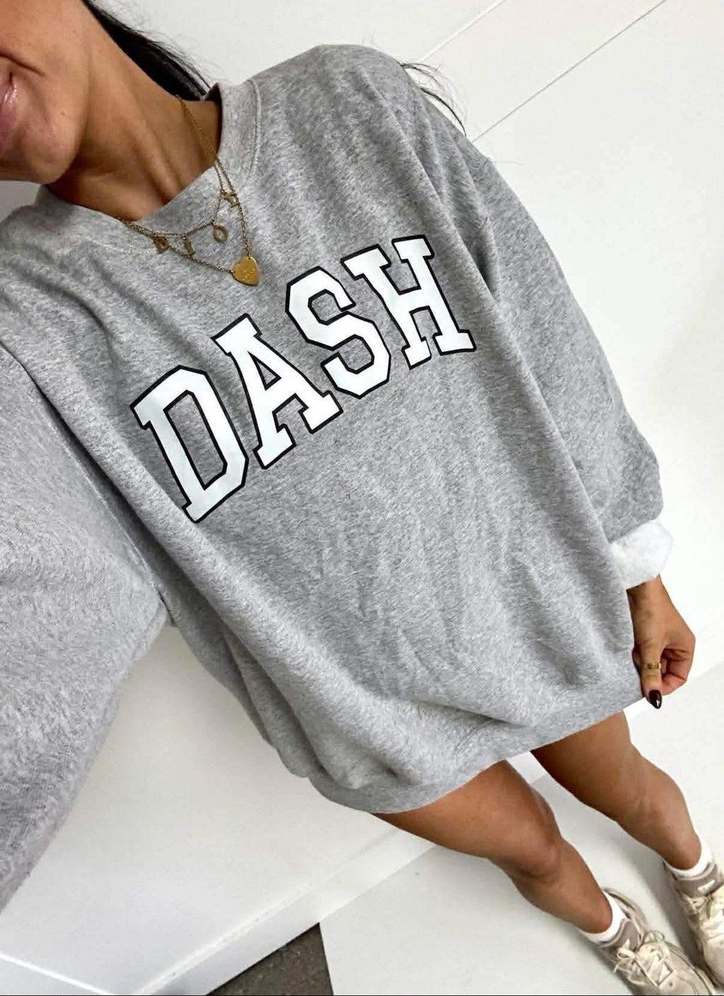 Person wearing a gray sweatshirt with 'DASH' printed on it, sitting on a white surface.