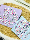Two fabric letters, one purple and one light blue, with floral patterns on a woven surface.