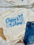White t-shirt with 'Coffee & Jesus' text and blue stripes, paired with denim shorts on a light background.