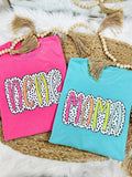 Two colorful t-shirts with 'New Mom' text on a textured surface.