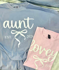 Two shirts, one blue and one pink, with 'aunt est. 2026' and 'lovey est. 2026' text.