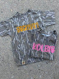 Two camouflage-patterned shirts with names 'Beckham' and 'Kolbie' on a concrete surface.
