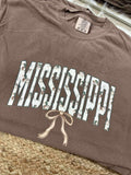 Brown t-shirt with 'Mississippi' printed on it, featuring a bow design, on a woven surface.