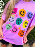 Person wearing a purple t-shirt with colorful pumpkin designs outdoors.