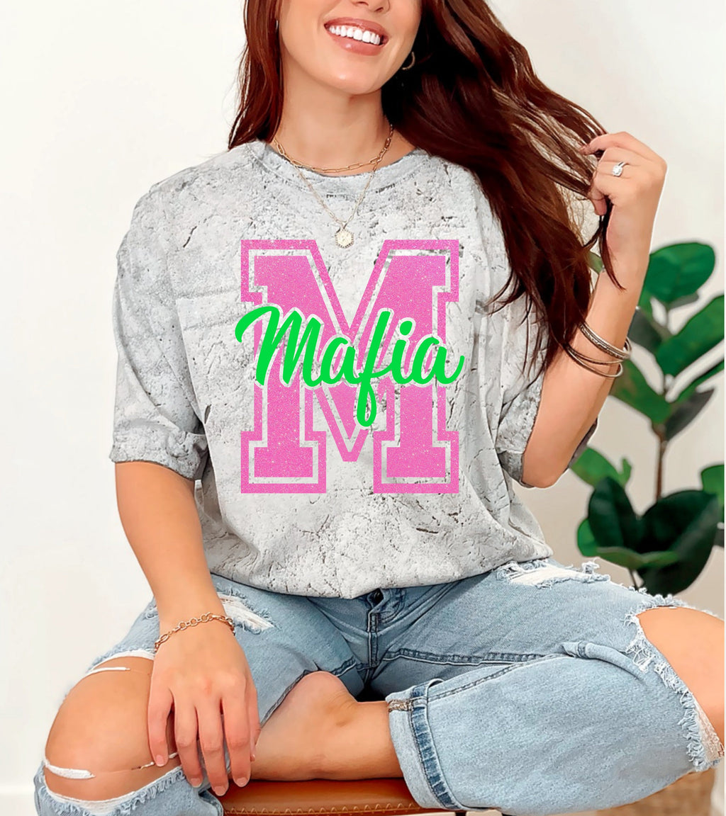 Woman wearing a gray oversized shirt with 'Mafia' print, sitting on a white background.