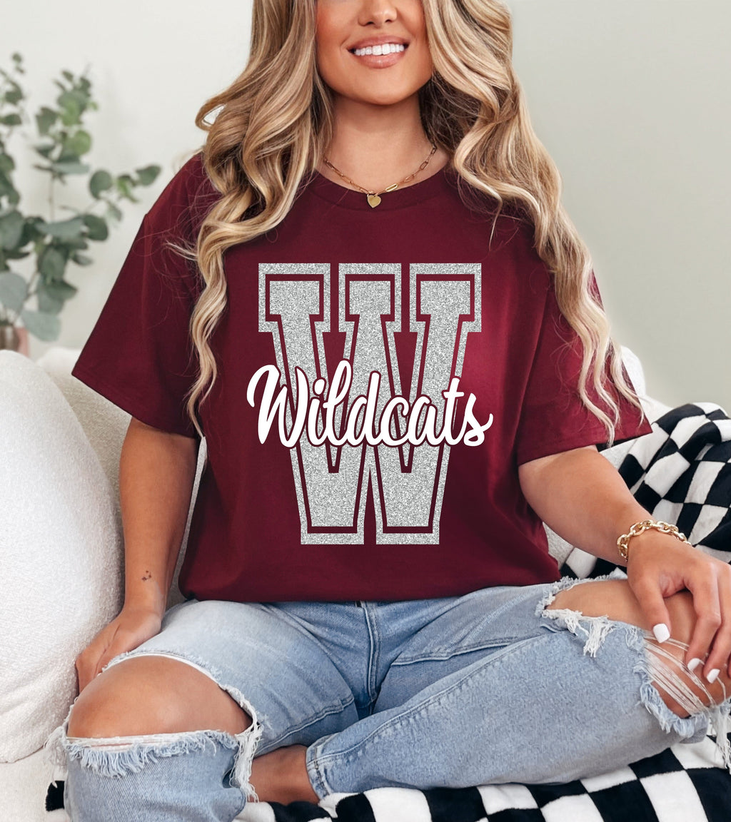 Person wearing a maroon t-shirt with 'Wildcats' printed on it, sitting on a checkered blanket.